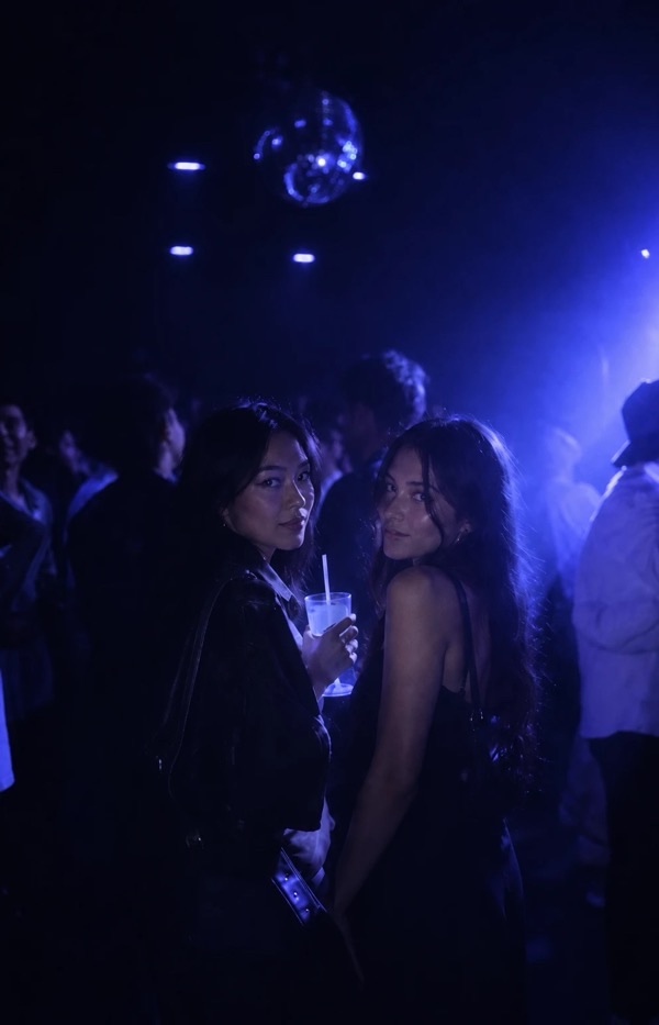 Two friends looking back at the camera on a dark dance floor, a disco ball above them.